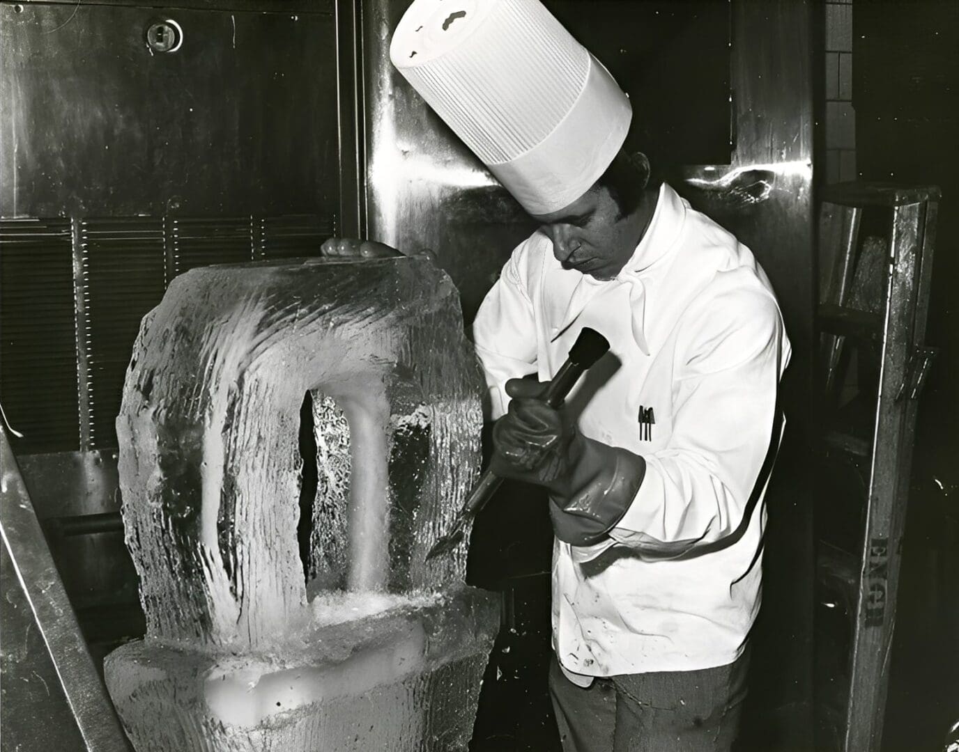 Chef carving ice sculpture with chisel.